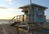 海滩上的 lifeguard tower 贴着注意离岸流的警示牌