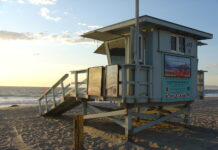 海滩上的 lifeguard tower 贴着注意离岸流的警示牌