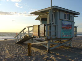 海滩上的 lifeguard tower 贴着注意离岸流的警示牌