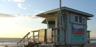 海滩上的 lifeguard tower 贴着注意离岸流的警示牌