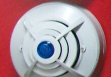美国消费品安全委员会警告立即停用约376974台KH158插电式四合一天然气与一氧化碳报警器,已知91起未能报警报告 安装在红色墙面上的圆形家用报警器示意,并非被点名的KH158型号