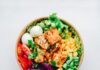 一份配有豆腐、生菜、玉米与番茄的健康餐碗，配图说明美国农业部加码校园餐与本地农产品对接，并非某一所学校的实际供餐现场