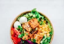 农业部与卫生部8月24日推出Harvest to Hallways:校园厨房最多7000万美元、农场到学校再加2500万美元 一份配有豆腐、生菜、玉米与番茄的健康餐碗,配图说明美国农业部加码校园餐与本地农产品对接,并非某一所学校的实际供餐现场